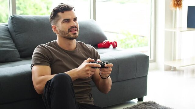 A hadsome guy is sitting playing a video game on a playstation at home. Stay at home,  Man playing with a videogame controller in his hands.