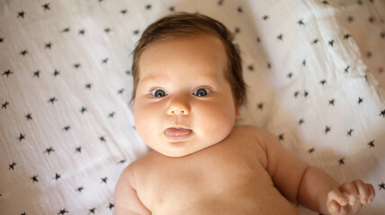 Little infant child lying on back on blanket and showing tongue. Portrait of baby girl with funny...