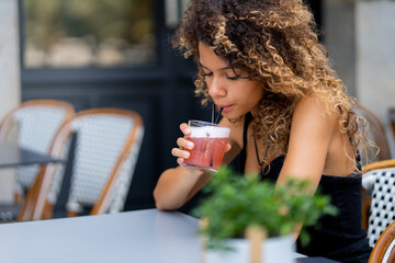 Young woman drinking red cocktail at the bar terrace using straw