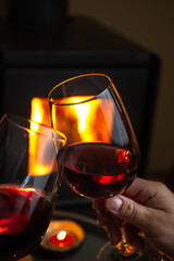 Two person holding glasses of red wine front of fireplace. Romantic light