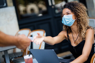 Young woman wearing face mask taking bill at a café terrace