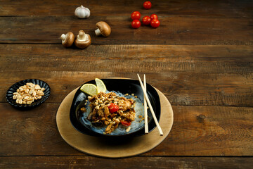 A plate of funchoses with chicken and vegetables in pad Thai sauce sticks on a stand next to vegetables.