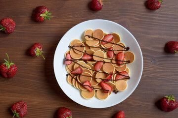 Mini pancakes with strawberries and chocolate lie on a wooden table.