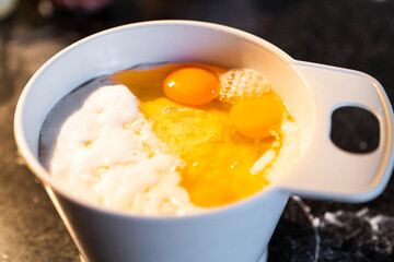 White recipient full of flour and eggs to make a cooking recipe. Preparation of a homemade cake at home at night in warm light.