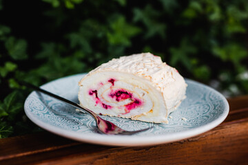 A meringue roll with raspberries on a blue plate with a fork in soft light