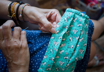 Old woman hand sewing fashion cotton fabric masks at home