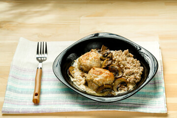 Chicken meatballs with mushrooms in a creamy sauce with green buckwheat in a black plate on a linen napkin.