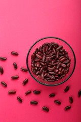 Glass jar with red beans on a pink background.