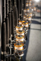Group of gold colored fishing poles with spools on fishing boat in hard sunlight