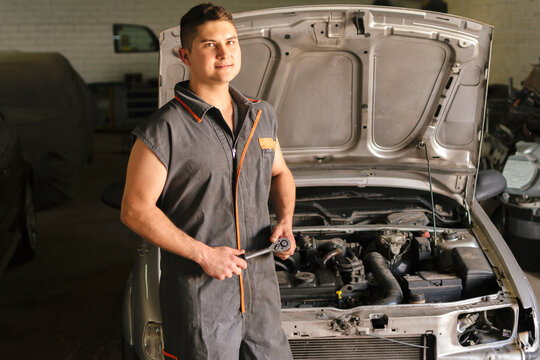 Mechanic looking straight ahead with a ratchet wrench with the hood of an open car in the background.