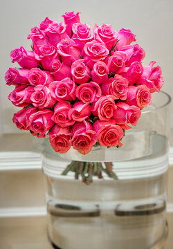 Large Bouquet Of Two Dozen Pink Roses In Large Glass Vase With Water Against White  Background