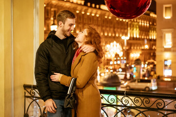 A happy couple stands in an embrace on the street in the evening in the festive lights