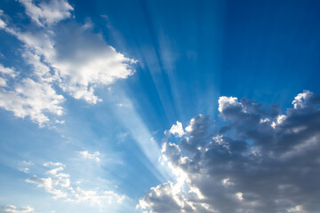 Rays of sunlight coming out from between the clouds in an intense blue sky