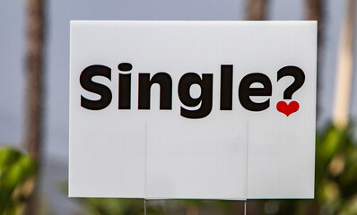 Sign with the word SINGLE and a question mark with a heart with palm tree trunks in background