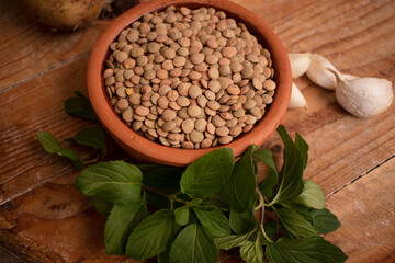 Lentils in bowl, fresh mint and garlic on wooden background