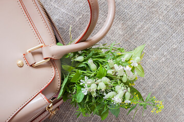 Bouquet of meadow flowers sticking out of female leather handbag closeup. Concept of gifts, holidays, shopping
