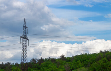 Obraz premium High voltage pole with wires against a cloudy sky and forest