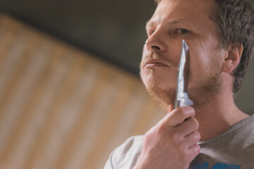 A man shaving himself with a knife.