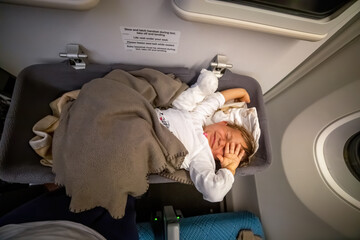 infant passenger toddler wakes up on the airplane and stretches in special baby bassinet
