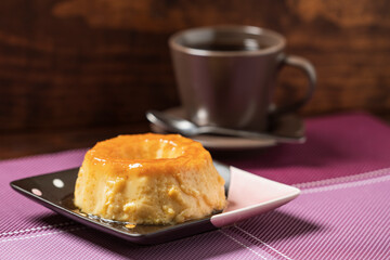 Delicious Caramel Flan on a square plate and a purple placemat. Wooden background
