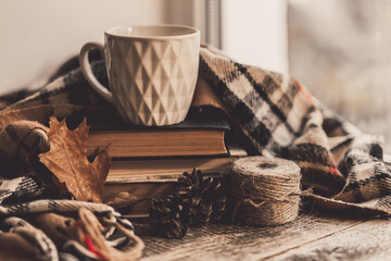 Details of still life on window. Book with scarf and cup of tea on wood background. Autumn mood.
