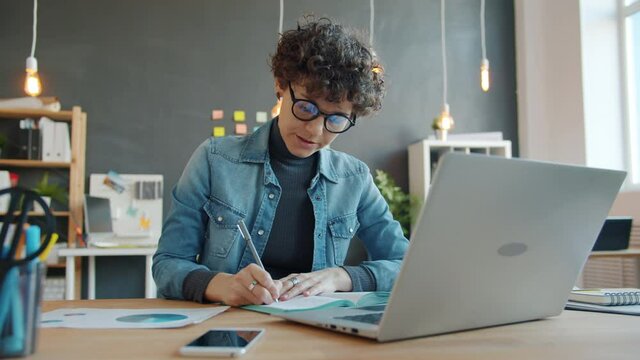 Female entrepreneur is writing at desk in office working alone planning business taking notes about ideas. People, job and modern lifestyle concept.