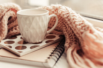 Details of still life on window. Beautiful pink mug of tea with notebook and knitted scarf. Pink mood.