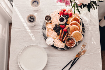 Breakfast platter. Table setting. Pancakes, breakfast sausages, berries, fruits, chocolate spread and coffee. Morning light. White and grey colors. Peonies. Summer time. Sunday brunch party. Weekend