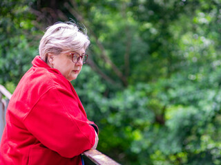A Mature sad woman in glasses and a red jacket is resting in a city Park