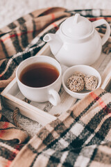Cup of hot drink and teapot on a serving tray, knitting clothes. Cozy autumn or winter concept.