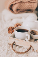 Cup of hot drink and teapot on a serving tray, knitting clothes. Cozy autumn or winter concept.