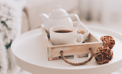Cup of hot drink and teapot on a serving tray on table. Cozy autumn or winter concept.