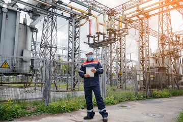 An electrical substation engineer inspects modern high-voltage equipment in a mask at the time of pondemia. Energy. Industry