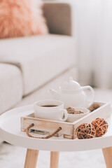 Cup of hot drink and teapot on a serving tray on table. Cozy autumn or winter concept.