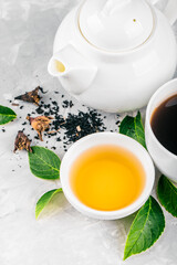 Herbal tea, cups and teapot with leaves on grey concrete background. Flat lay.