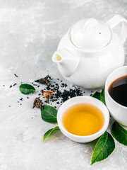 Herbal tea, cups and teapot with leaves on grey concrete background. Flat lay.