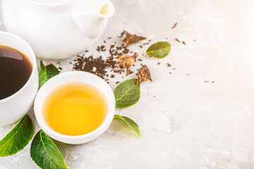 Herbal tea, cups and teapot with leaves on grey concrete background. Flat lay.