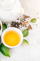Herbal tea, cups and teapot with leaves on grey concrete background. Flat lay.