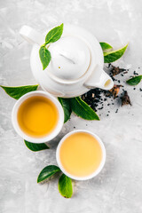 Herbal tea, cups and teapot with leaves on grey concrete background. Flat lay.