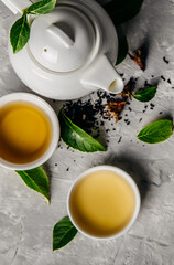 Herbal tea, cups and teapot with leaves on grey concrete background. Flat lay.