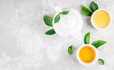Herbal tea, cups and teapot with leaves on grey concrete background. Flat lay.
