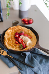 Dutch baby pancake baked until golden brown in cast iron skillet and topped with strawberries, banana and maple syrup. Weekend brunch meal. Sunday breakfast. Simple recipe. Fluffy battered pancake.