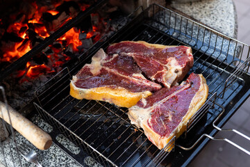 Close-up three big tasty juice raw t-bone beaf steak on grill at barbecue with bright hot burning charcoal at brazier. BBQ meal cooking background
