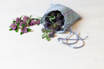 Cotton sachet bag with dry red clover flowers and fresh herbs on white wooden background