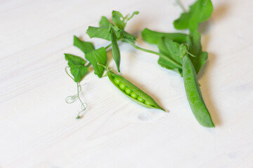 fresh green peas in pods with leaves on white wooden table