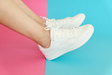 White women's sneakers dressed by a girl on a pink-blue background