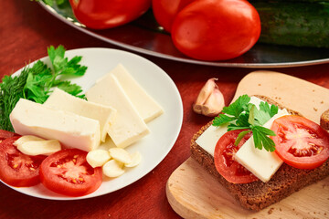 healthy food - fresh bread and feta cheese on a wooden background, tomatoes, greens and vegetables