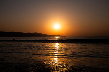 Naklejka premium Sunset or sunrise, on the coast of the sea or the ocean, in the distance you can see mountains