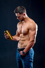Portrait of a handsome halfnacked bodybuilder man with a sport bottle of water. Man posing on dark...