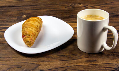 Cup of fresh coffee and baked croissants on a wooden background.